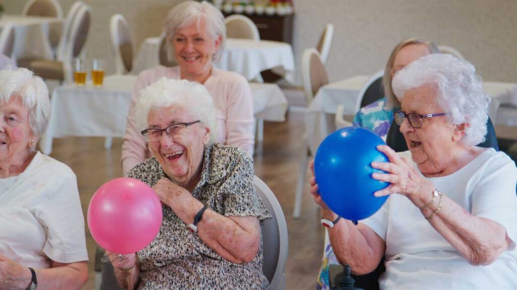 Two seniors smiling as they chat with a family member on a video call using a tablet in a cozy living room.