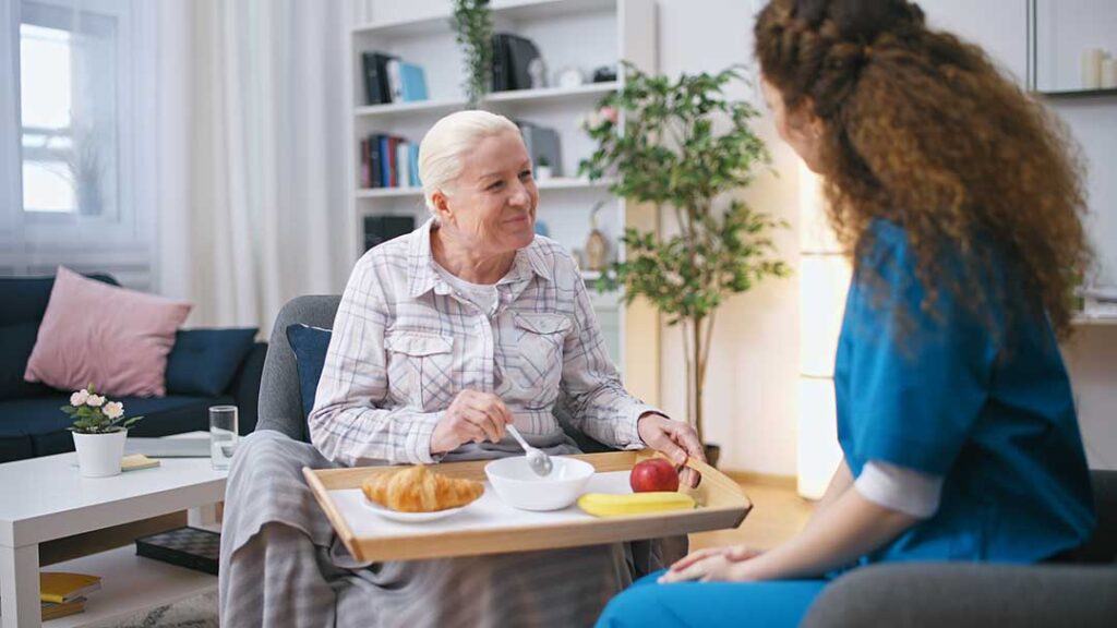 Older adults sitting together at a sunlit table, sharing conversation and reading printed materials.