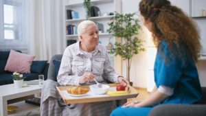 Older adults sitting together at a sunlit table, sharing conversation and reading printed materials.