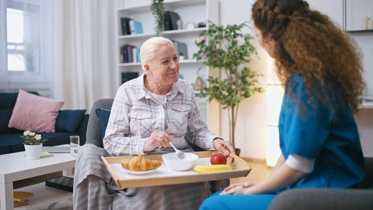 Older adults sitting together at a sunlit table, sharing conversation and reading printed materials.